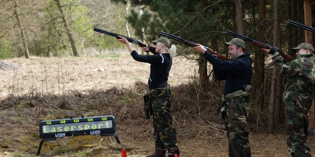 People aiming shotguns for laser clay shooting in the forest